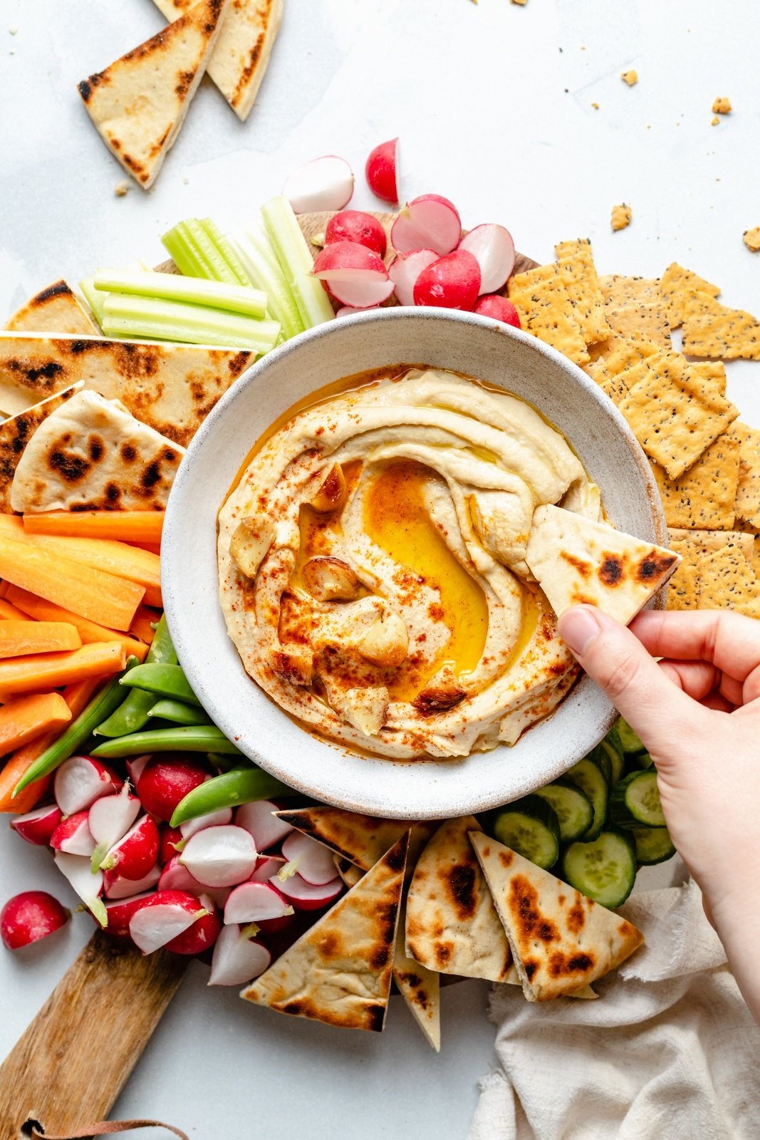 dipping pita into a bowl of roasted garlic hummus surrounded by veggies